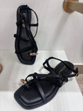 Black flat leather sandals with thin straps and gold ring detail on the front strap.