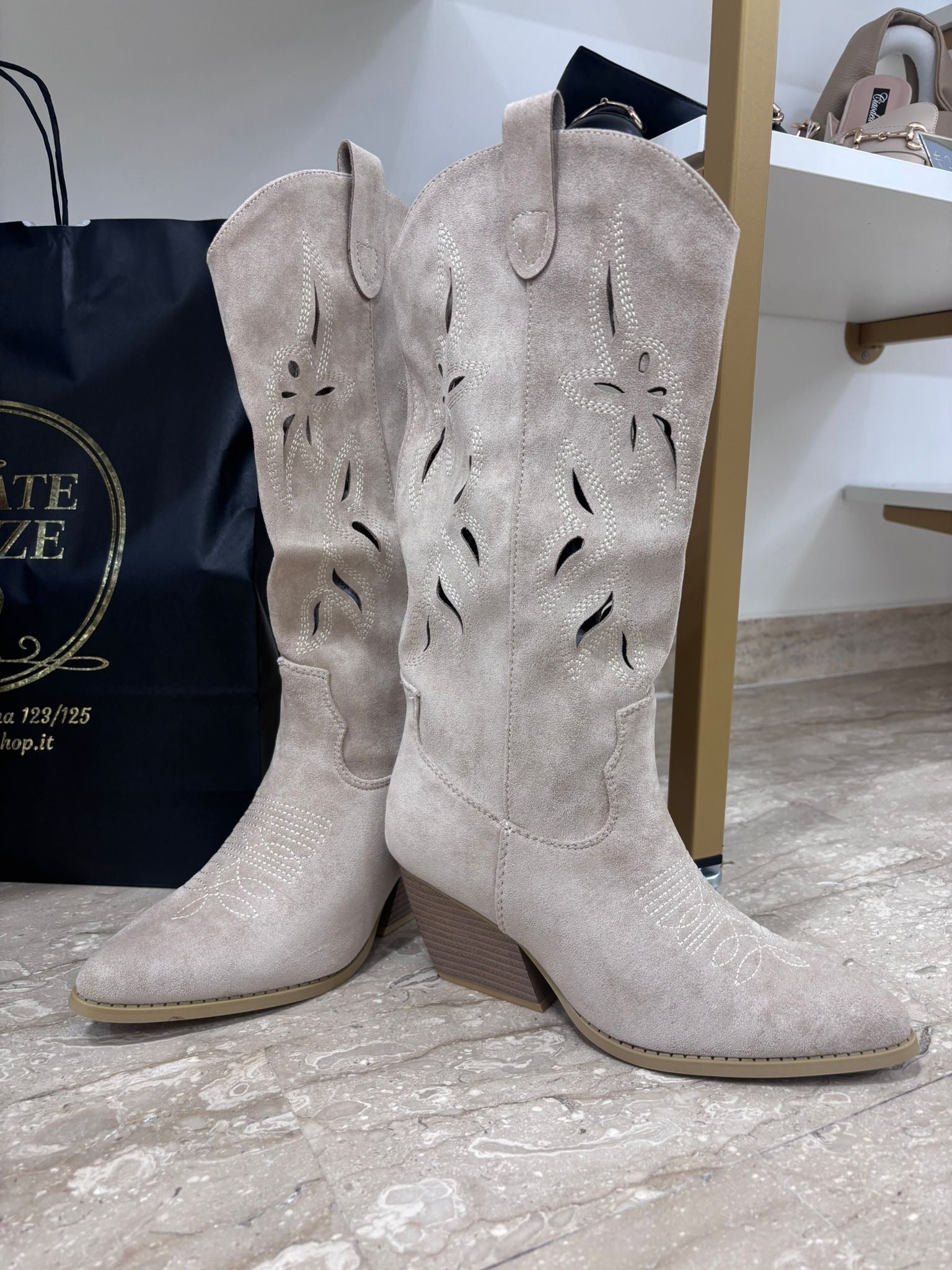 Beige suede western-style mid-calf boots with laser-cut floral patterns and pointed toes.