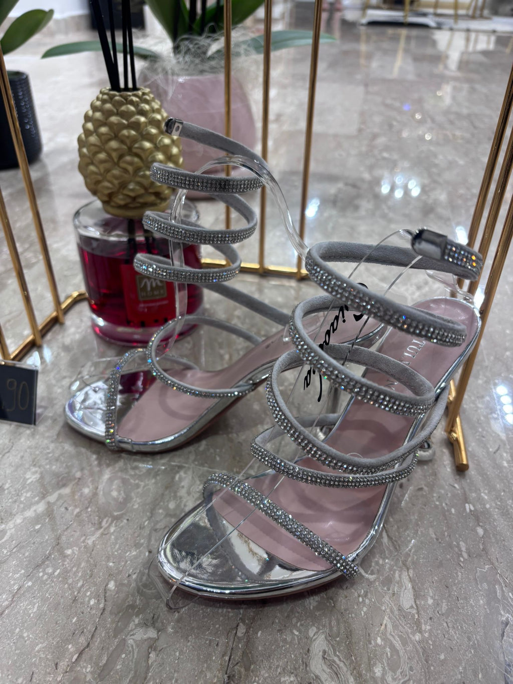Silver high-heeled sandal with multiple thin straps and an ankle buckle on a marble floor.