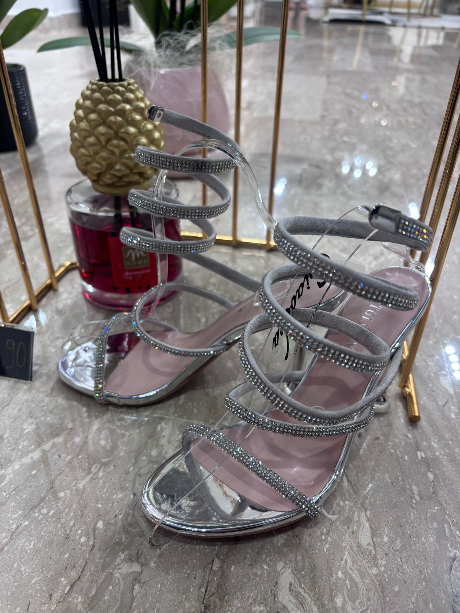 Silver high-heeled sandal with multiple thin straps and an ankle buckle on a marble floor.