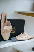 Beige open-back moccasin flats with gold chain detail on top, sleek minimalist design.