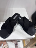 Black flat sandals with wide crossed leather straps and square toes on white surface.