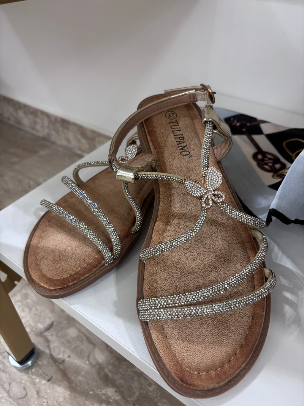 Gold flat leather sandals with strass butterfly detail and ankle strap.