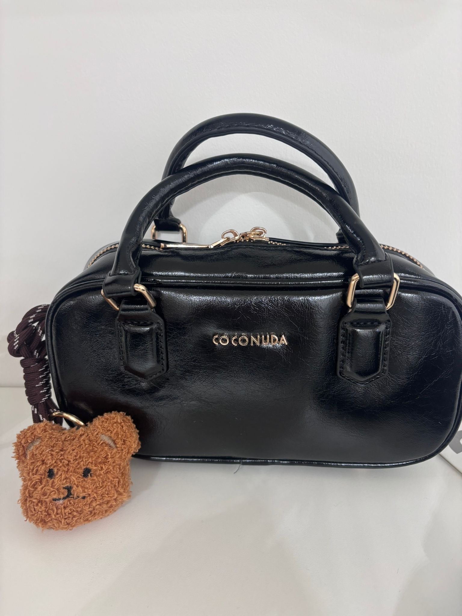 Black mini bag with rounded handles, gold zipper, COCO NUA logo, and a small brown teddy bear keychain.