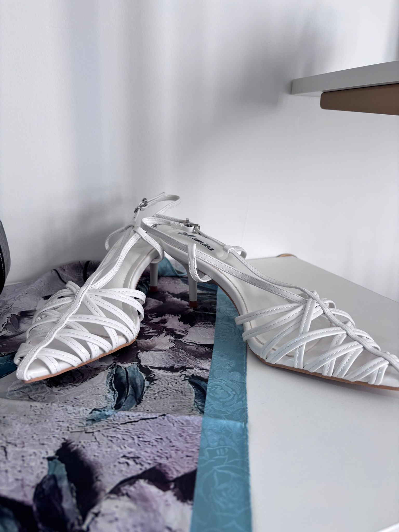 White slingback sandal with woven leather straps and low heel on white surface.