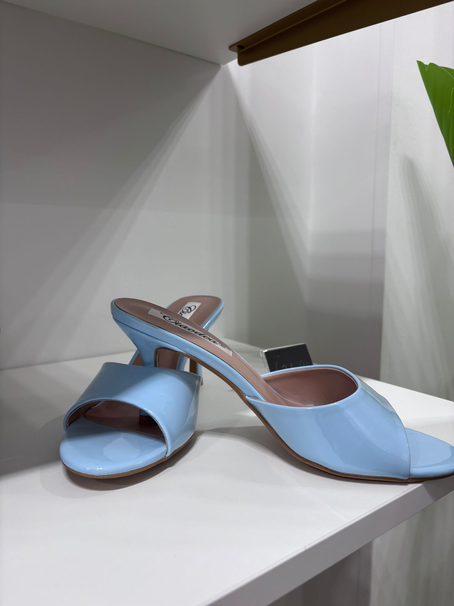 Light blue patent leather mules with open toe, block heel, and slip-on design on white surface.