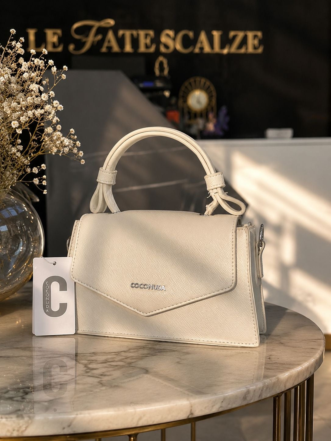 Cream leather mini lady bag with top handle and subtle gold logo detail on marble table.