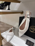 White pointed-toe ballerina flats with perforated design and slingback strap on display shelf.