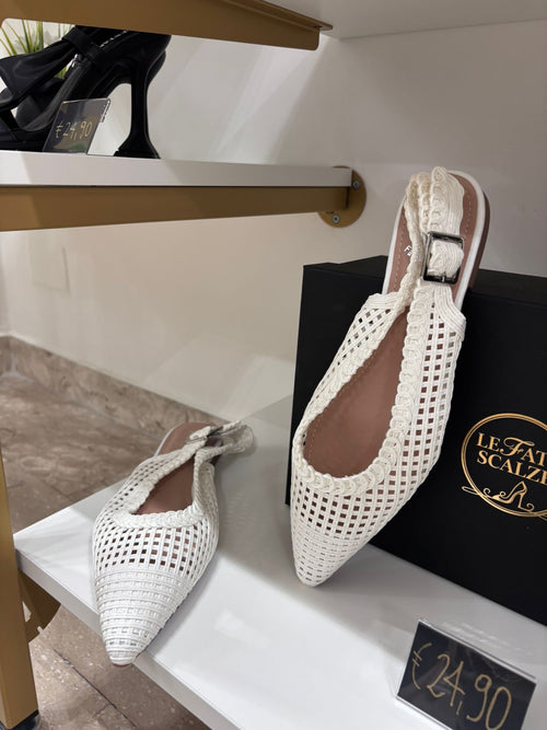 White pointed-toe ballerina flats with perforated design and slingback strap on display shelf.