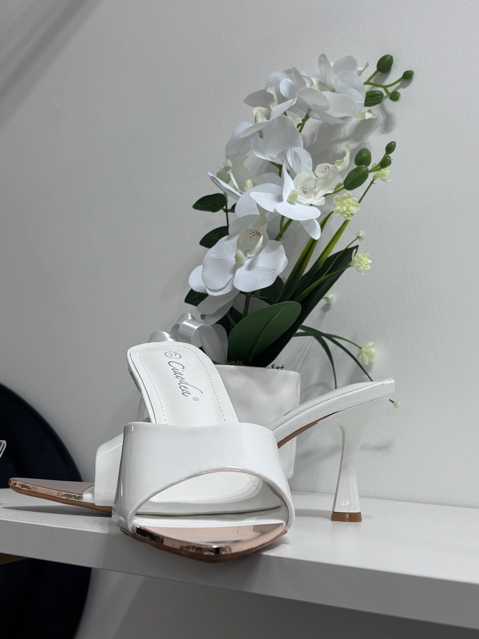 White glossy open-toe mule sandal with mid-height heel and slip-on design.