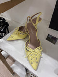 Yellow pointed-toe slingback flats with lace-up front and bow detail, smooth finish.