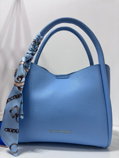 Sky blue textured leather handbag with rounded handles and a patterned silk foulard tied on one side.