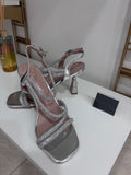 Silver strappy high-heeled sandals with double crystal embellishments and ankle straps on a white surface.