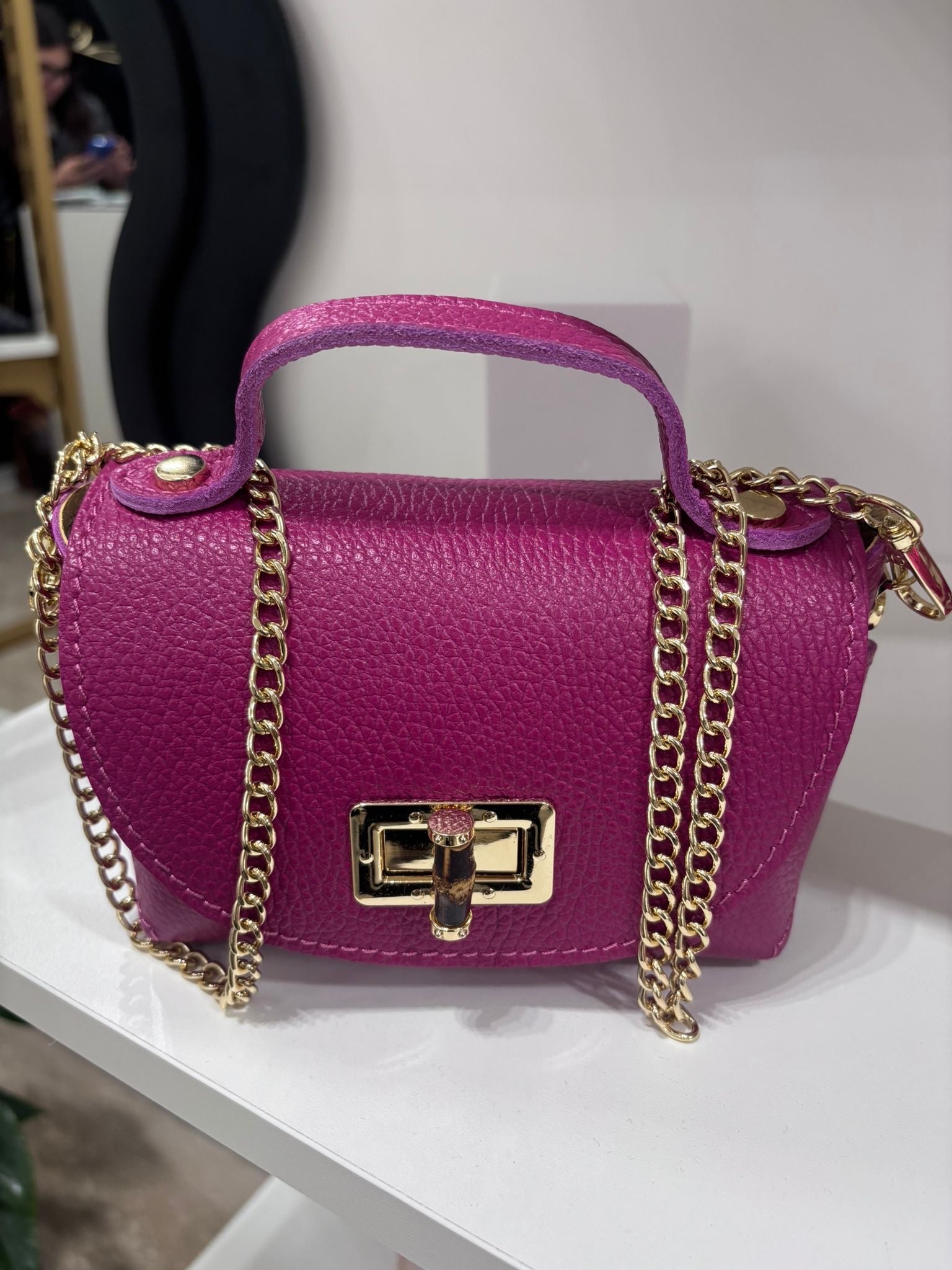 Fuchsia textured leather bag with gold chain strap and rectangular twist-lock closure.