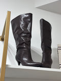 Tall brown leather boots with a soft, slightly slouched shaft and slim heels on a white shelf.