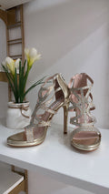 Gold strappy high-heeled sandals with rhinestone detailing and open toes on white surface.