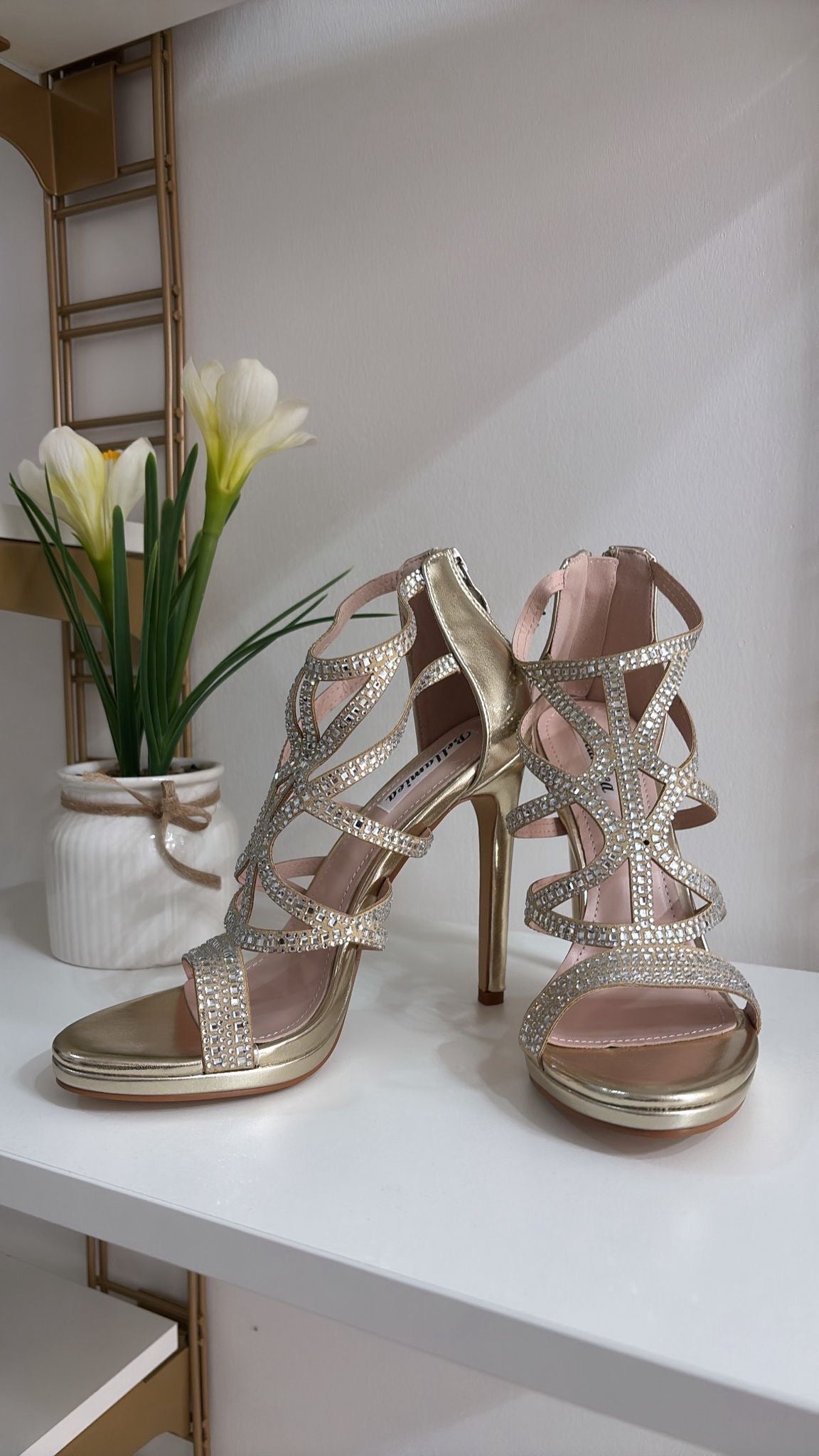 Gold strappy high-heeled sandals with rhinestone detailing and open toes on white surface.