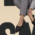 Black slingback flats with woven intreccio pattern and pointed toe on model wearing gray cropped pants.