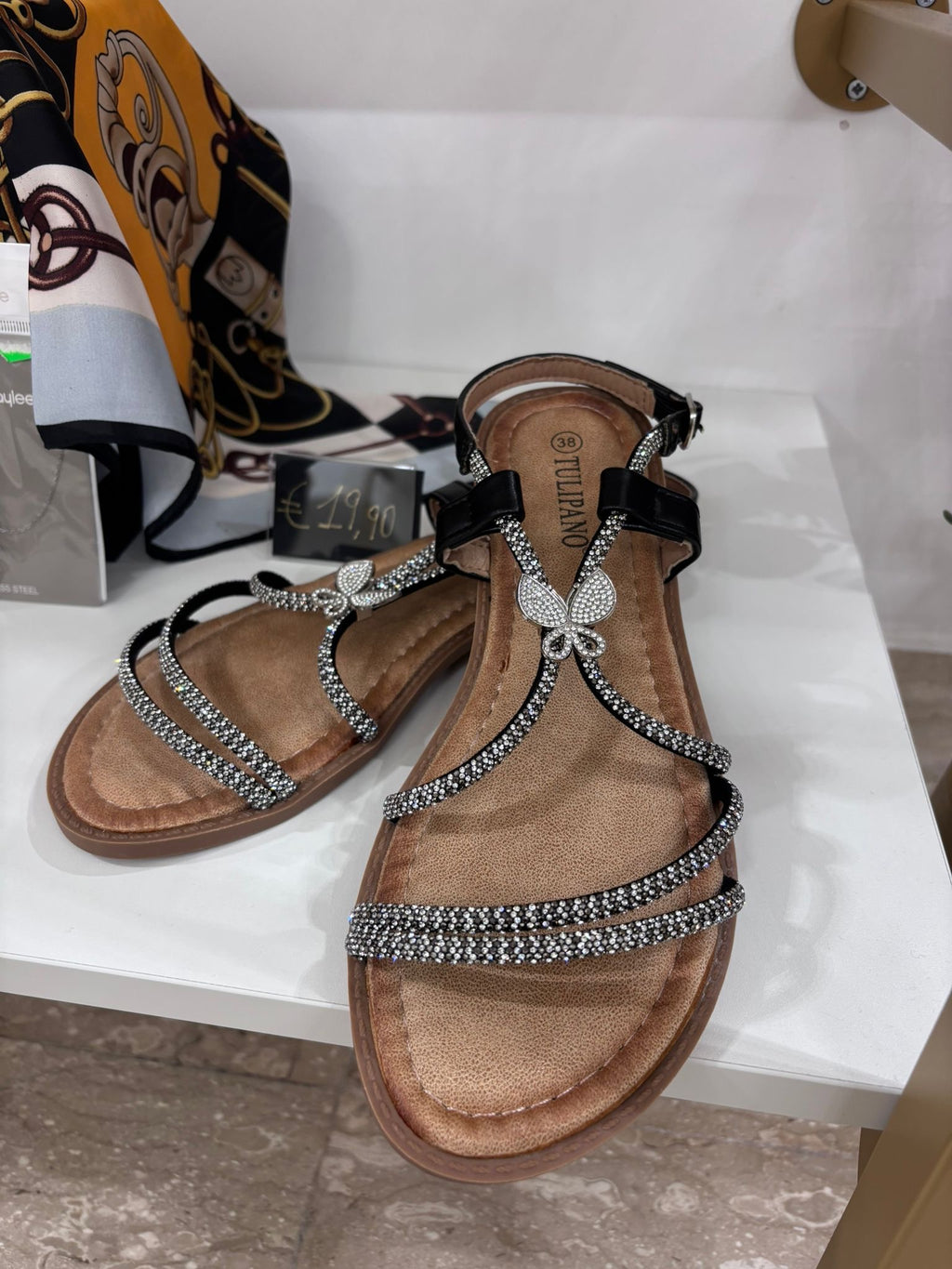 Black leather flat sandals with rhinestone straps and butterfly embellishment on the front.