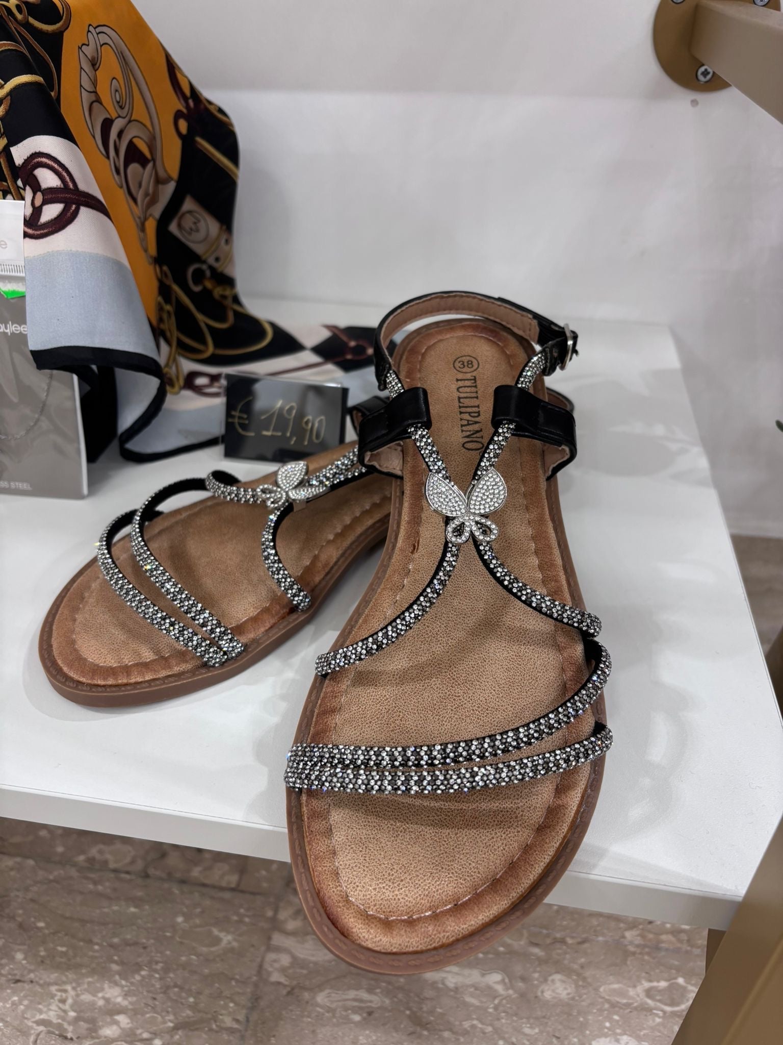Black leather flat sandals with rhinestone straps and butterfly embellishment on the front.