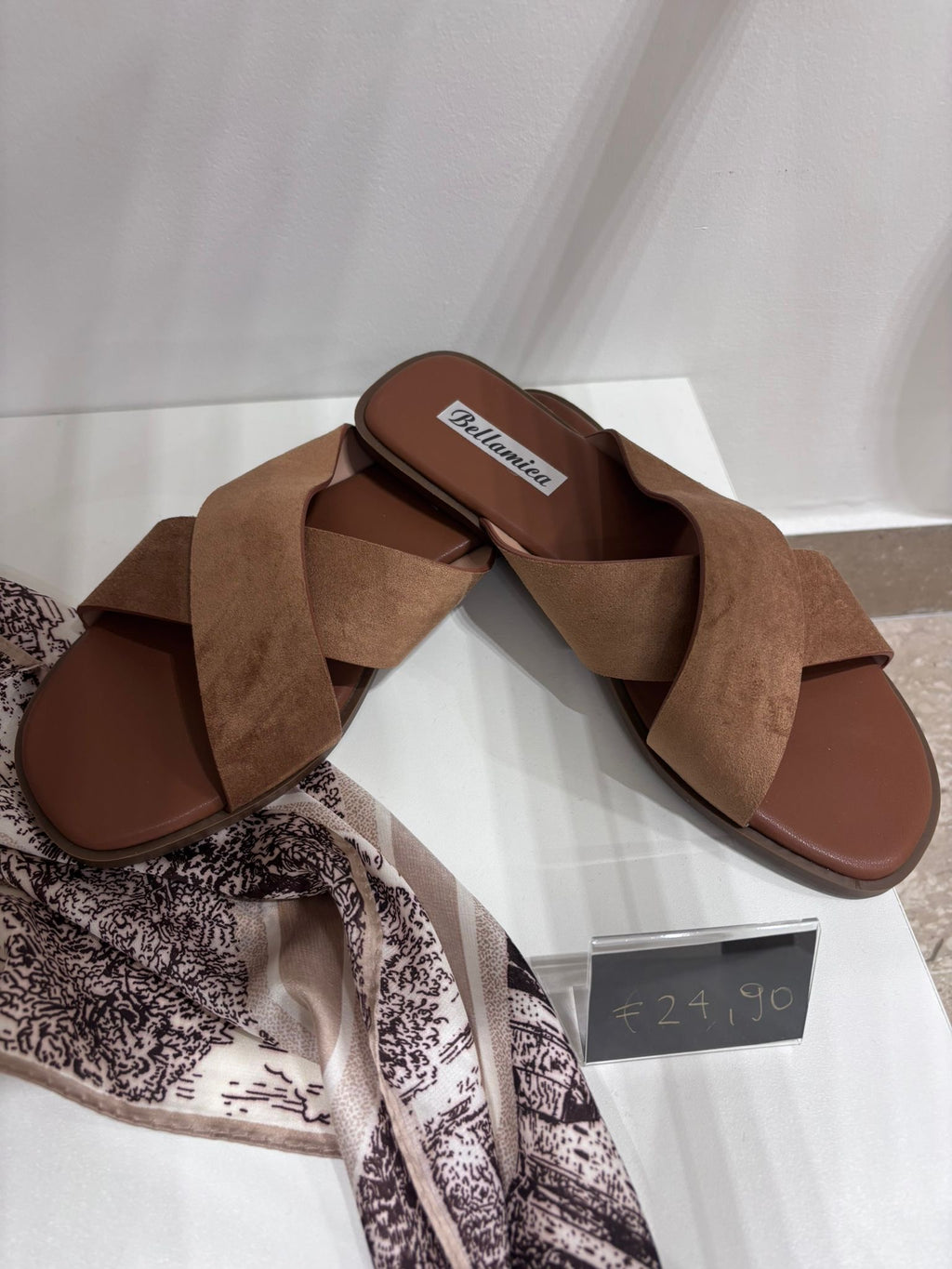 Brown suede flat sandals with wide crisscross straps and open toes on white display box.