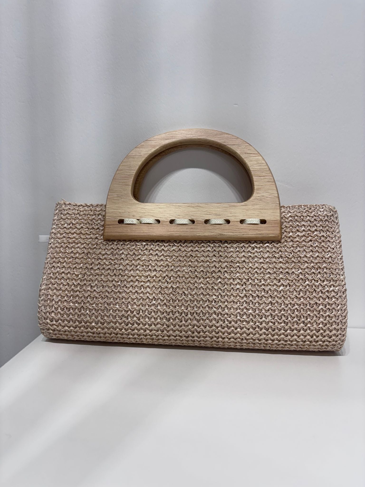 Beige woven straw clutch with curved wooden handle and rectangular shape.