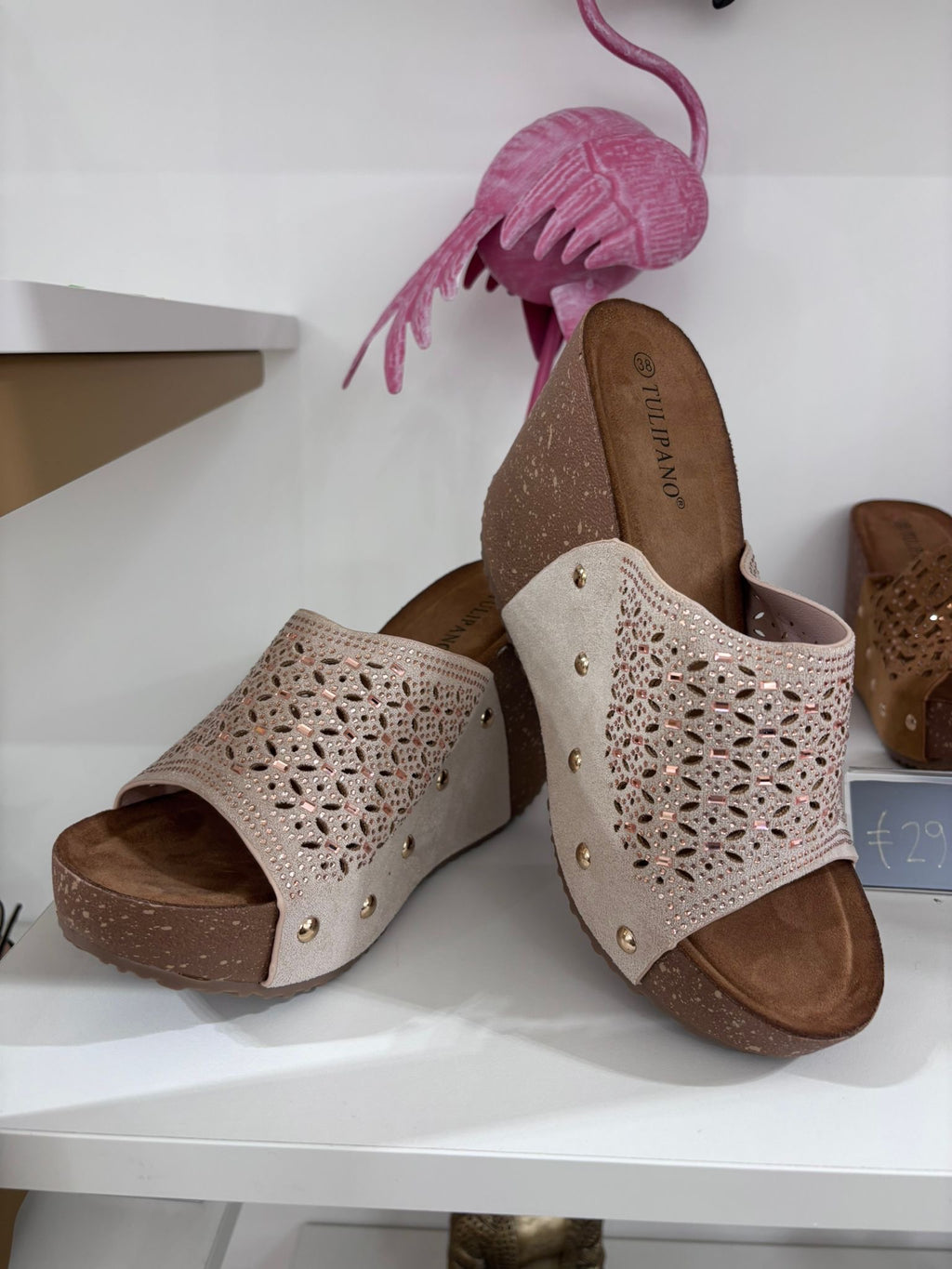Beige suede wedge sandals with perforated floral cutouts and open toes on a white display shelf.