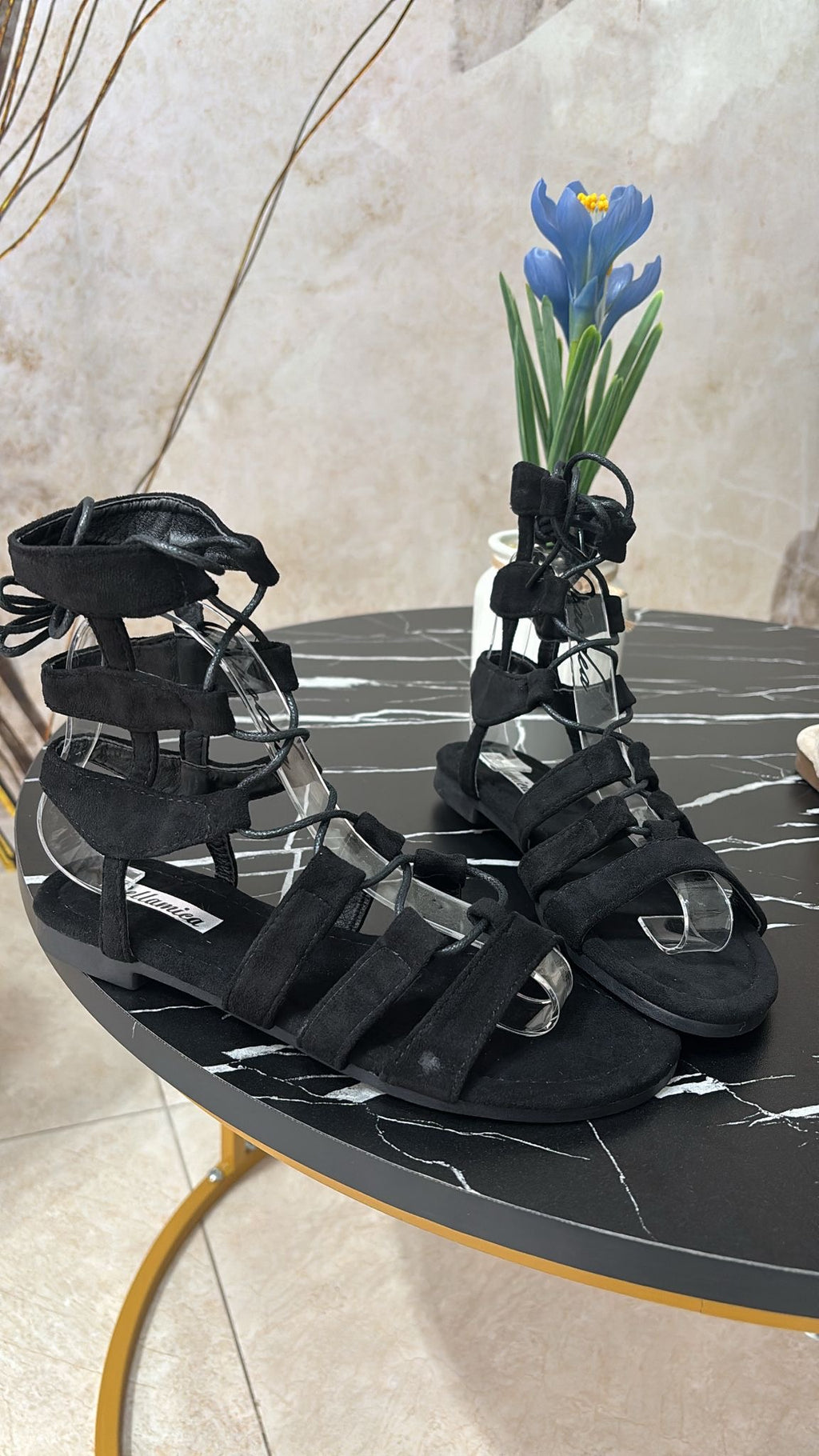 Black suede gladiator sandals with multiple straps and ankle ties on black marble table.