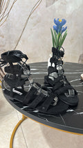 Black suede gladiator sandals with multiple straps and ankle ties on black marble table.
