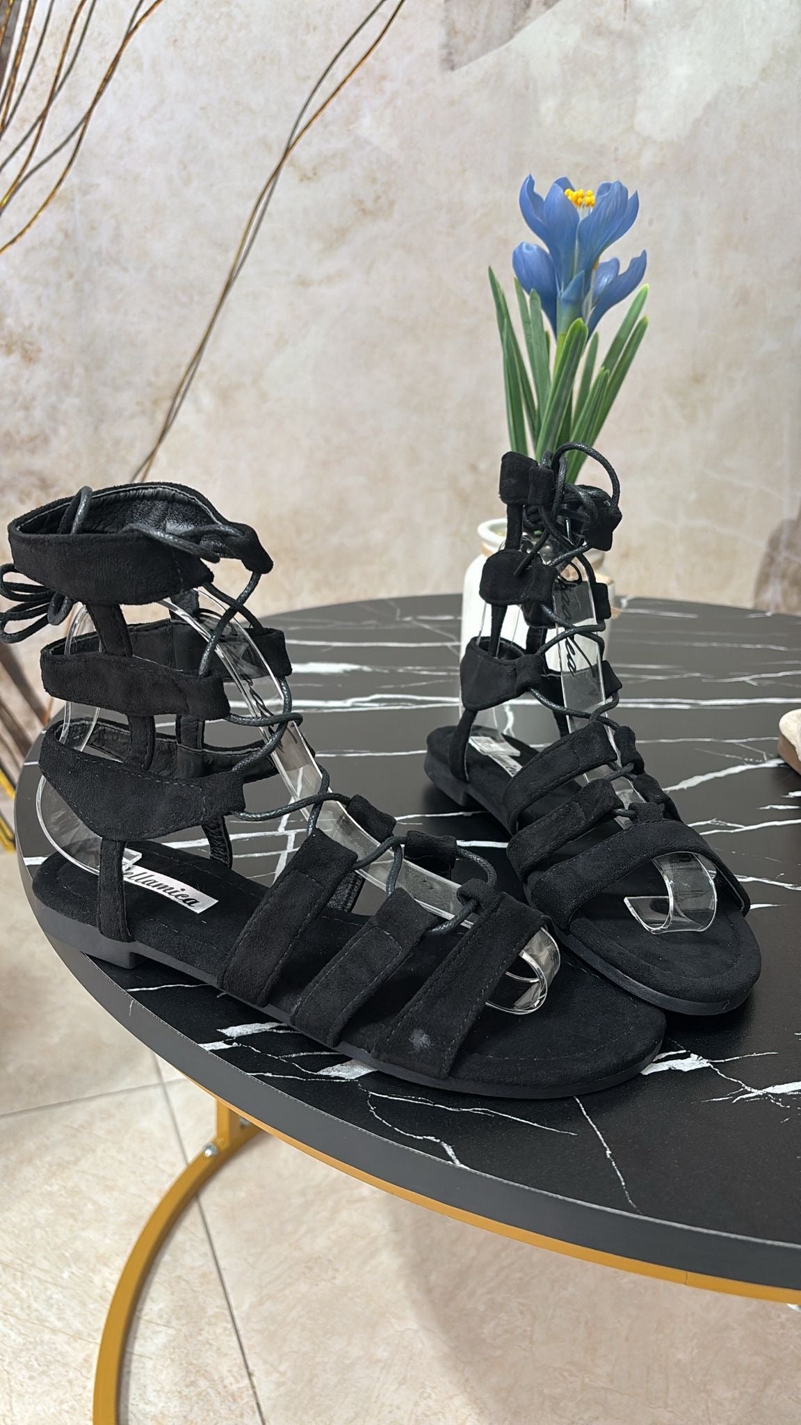Black suede gladiator sandals with multiple straps and ankle ties on black marble table.
