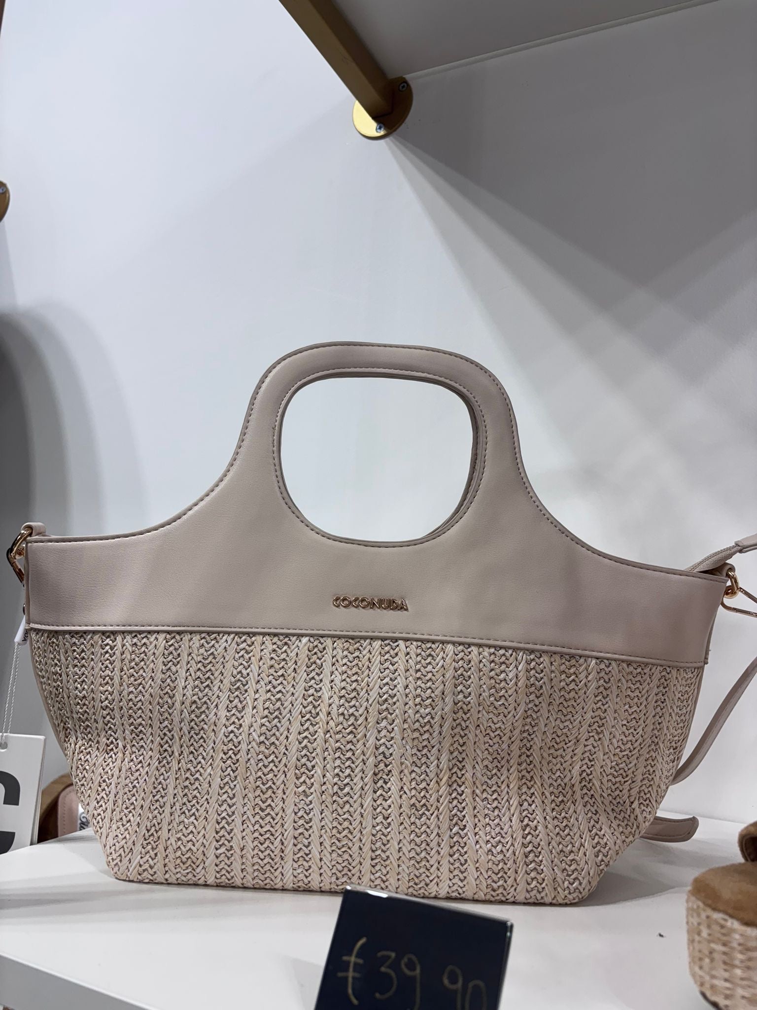 Beige structured tote bag with leather top, woven lower half, and cutout handles.