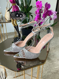 Silver high-heeled sandals with sparkling crystals, open toe, and ankle strap buckle on clear stand.